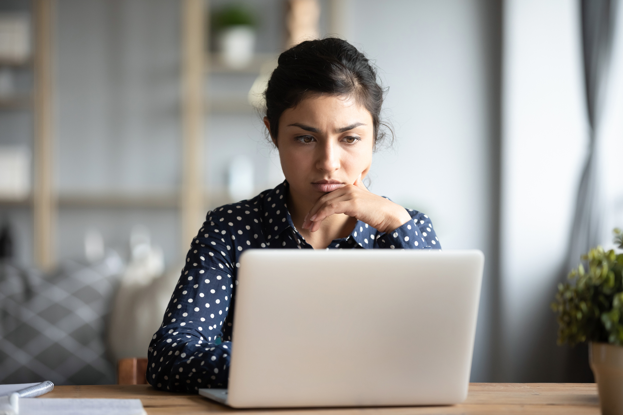 Woman with dark hair looks at laptop with concerned look on her face